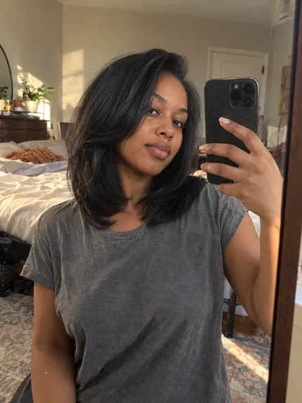 Woman with shoulder-length styled hair taking a bedroom mirror selfie
