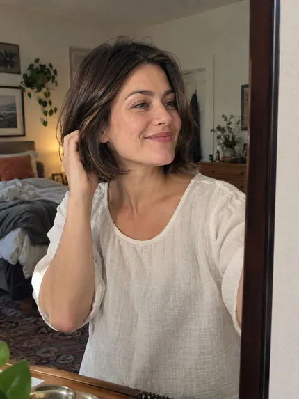 Woman with softly styled brunette bob in a bedroom mirror