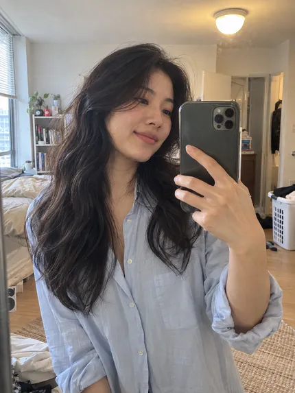 Woman with loose dark waves taking a bedroom mirror selfie