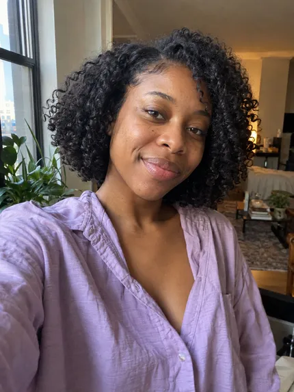 Woman with natural curls wearing a lavender shirt at home