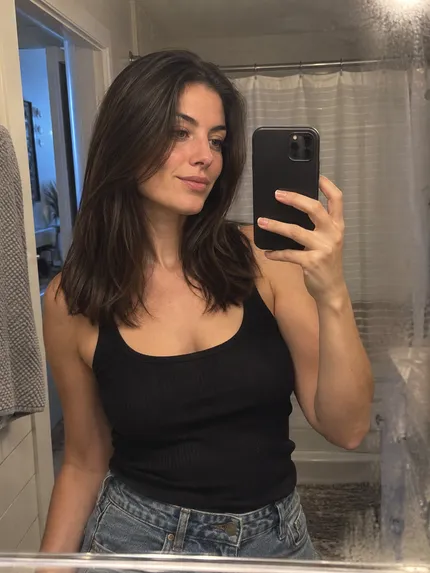 Woman with thick, softly straightened brunette hair taking a bathroom selfie